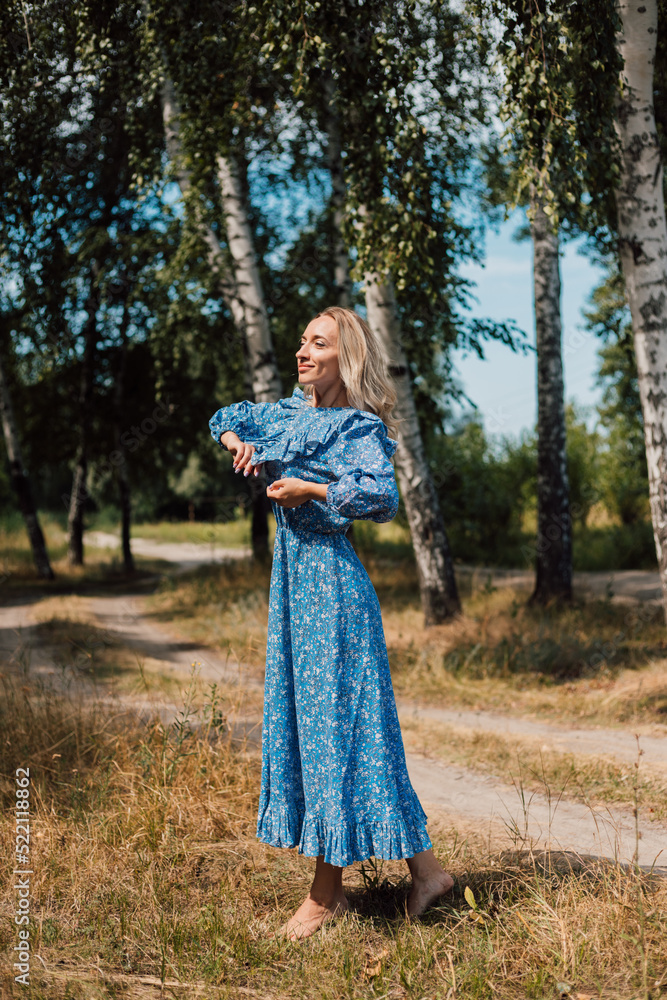 A young woman in a long dress stands in a clearing on a sunny summer day.