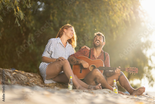 couple sitting on the beach playing song on guitar and laughing © Nemanja