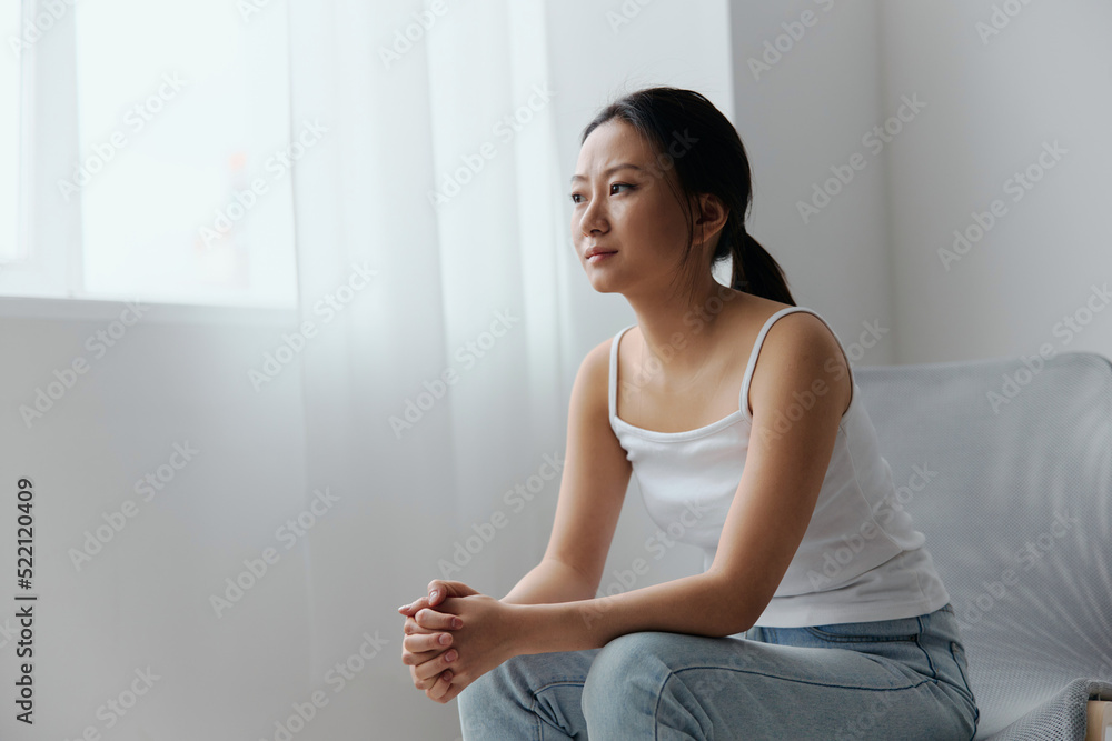 Sad thoughtful pensive frustrated tanned pretty young Asian woman recline on knee looks aside think about divorce at home interior living room. Injuries Poor health Illness concept. Cool offer Banner Sad thoughtful pensive frustrated tanned pretty young Asian woman recline on knee looks aside think about divorce at home interior living room. Injuries Poor health Illness concept. Cool offer Banner