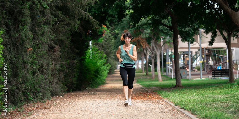 Middle aged woman running in the park in summer morning