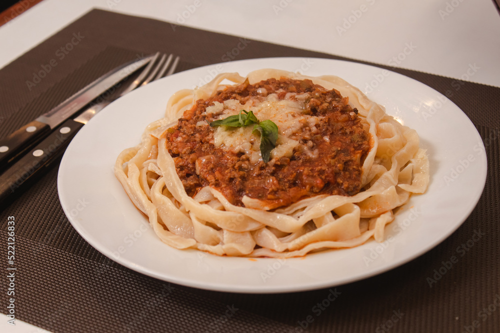 Detail view of a noodle with meat and sauce served on a white table Detail view of a noodle with meat and sauce served on a white table