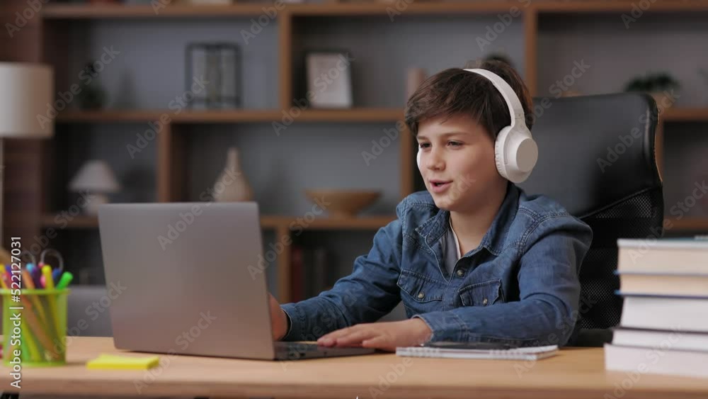 Schoolboy wearing earphones has online lesson, video call with teacher, answering questions, check of knowledge. Cute teenager studying at home using laptop. Distance learning and home education. Schoolboy wearing earphones has online lesson, video call with teacher, answering questions, check of knowledge. Cute teenager studying at home using laptop. Distance learning and home education.