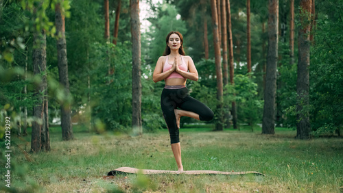 Vrikshasana. A young woman does yoga in the park, in the forest, in nature, she stands in the pose of a tree photo