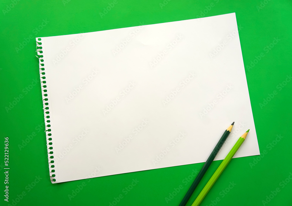 Blank sheet of paper space for design and lettering on a beautiful green background blue pencils. Perforated sheet torn from notepad obliquely lying on the surface. Square sheet of paper Blank sheet of paper space for design and lettering on a beautiful green background blue pencils. Perforated sheet torn from notepad obliquely lying on the surface. Square sheet of paper