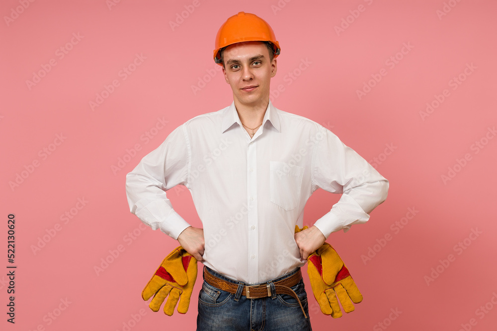 a young man in a white shirt and helmet put his hands on his belt and stands against a pink background