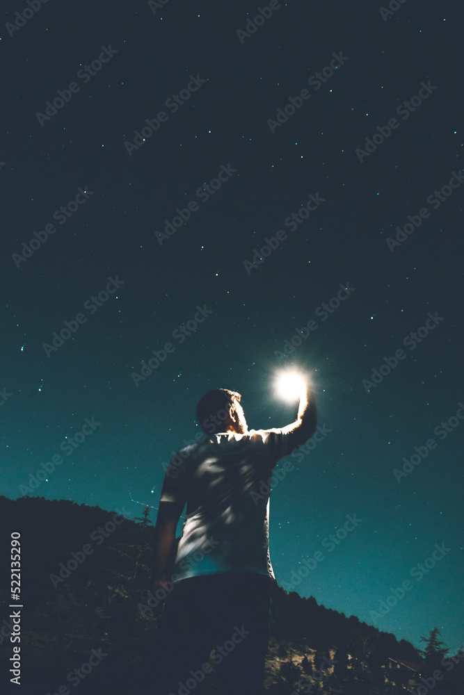 A young male looking at a star that he holds in hand at night A young male looking at a star that he holds in hand at night