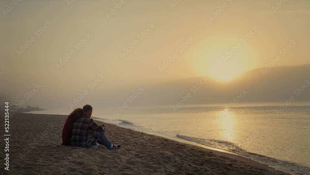 Loving couple sitting on sandy beach at ocean. Young lovers talking together