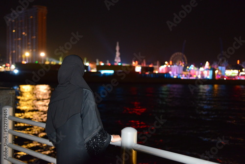 A young woman in a traditional black veil is looking at a festival of performing arts and culture at Jeddah, this festival was representing the vision 2030 of royal crown prince Muhammad Bin Salman photo