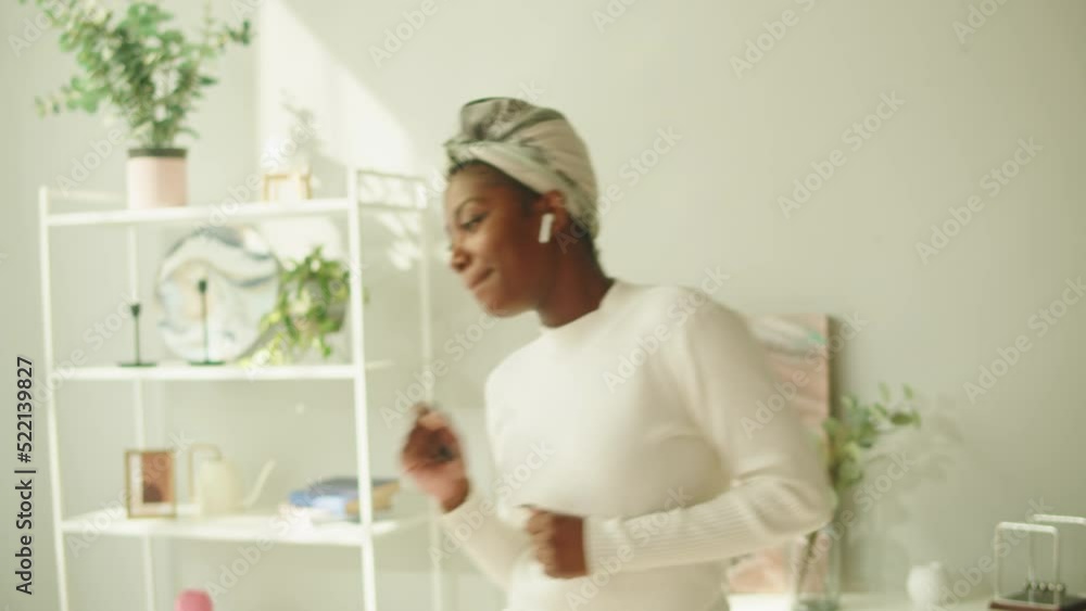 Happy native African woman dancing. Young female student having fun in living room, dance and smiling. Beautiful person listening to music in earphones, disco at home, wearing headscarf. Happy native African woman dancing. Young female student having fun in living room, dance and smiling. Beautiful person listening to music in earphones, disco at home, wearing headscarf.