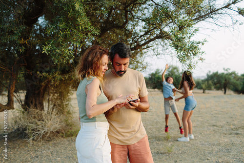 Mother and father looking at the phone with their children behind them photo