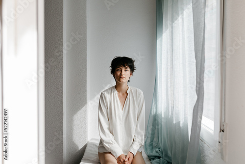 Tranquil androgynous person looking at camera in white room