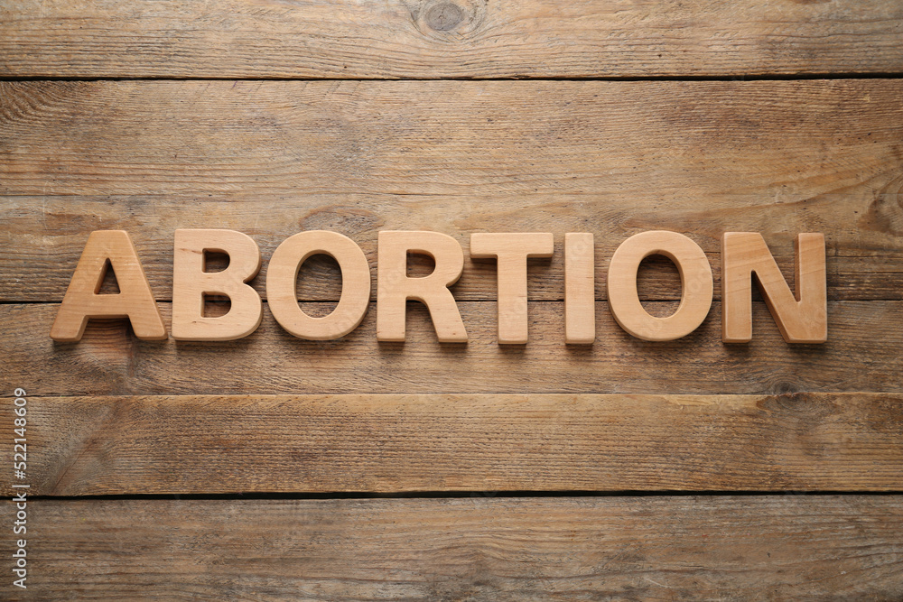 Word Abortion made of letters on wooden background, flat lay