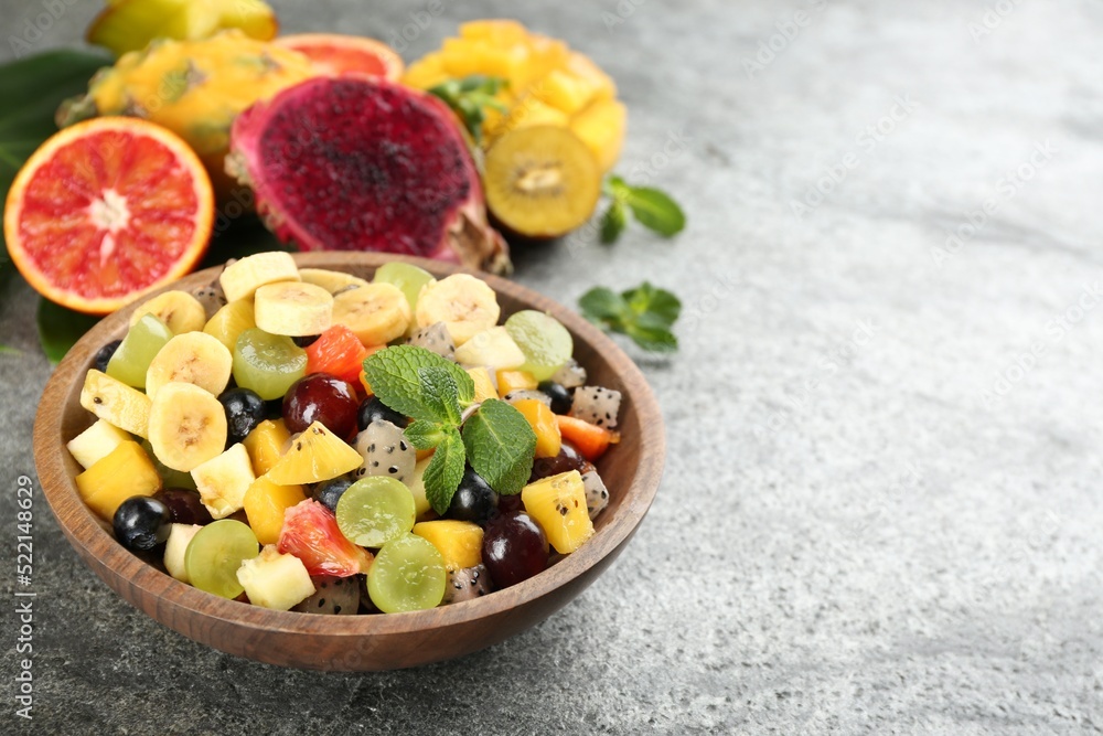 Delicious exotic fruit salad and ingredients on grey table. Space for text