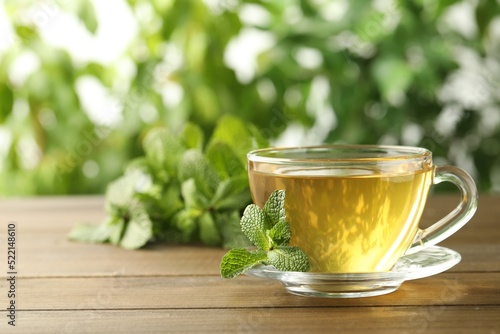 Glass cup of aromatic green tea with fresh mint on wooden table against blurred background. Space for text