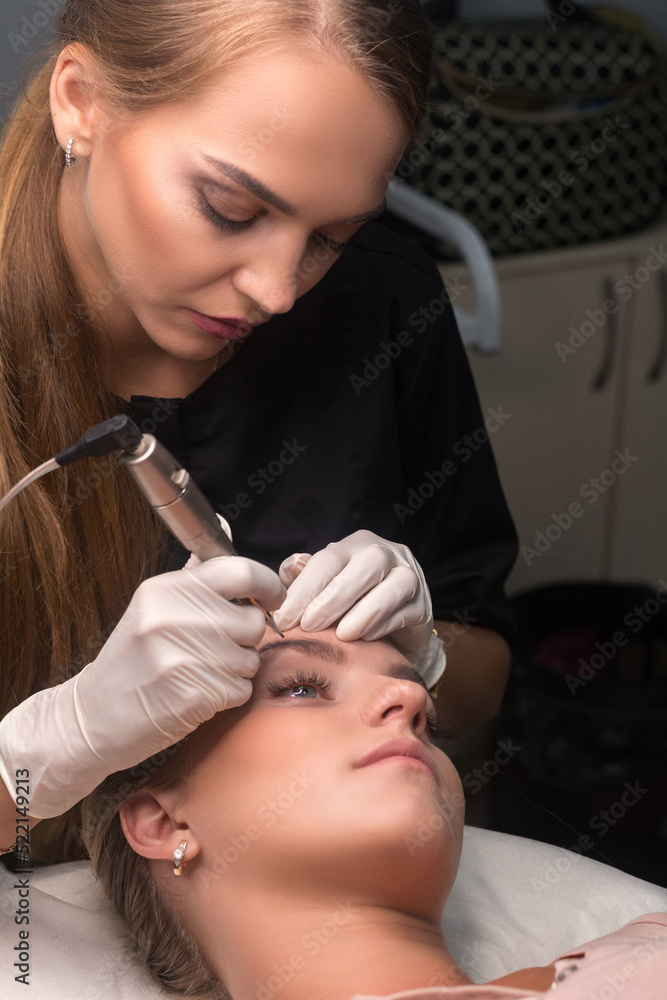 Fototapeta premium Permanent eyebrow makeup. Cosmetologist applying tattooing of eyebrows.