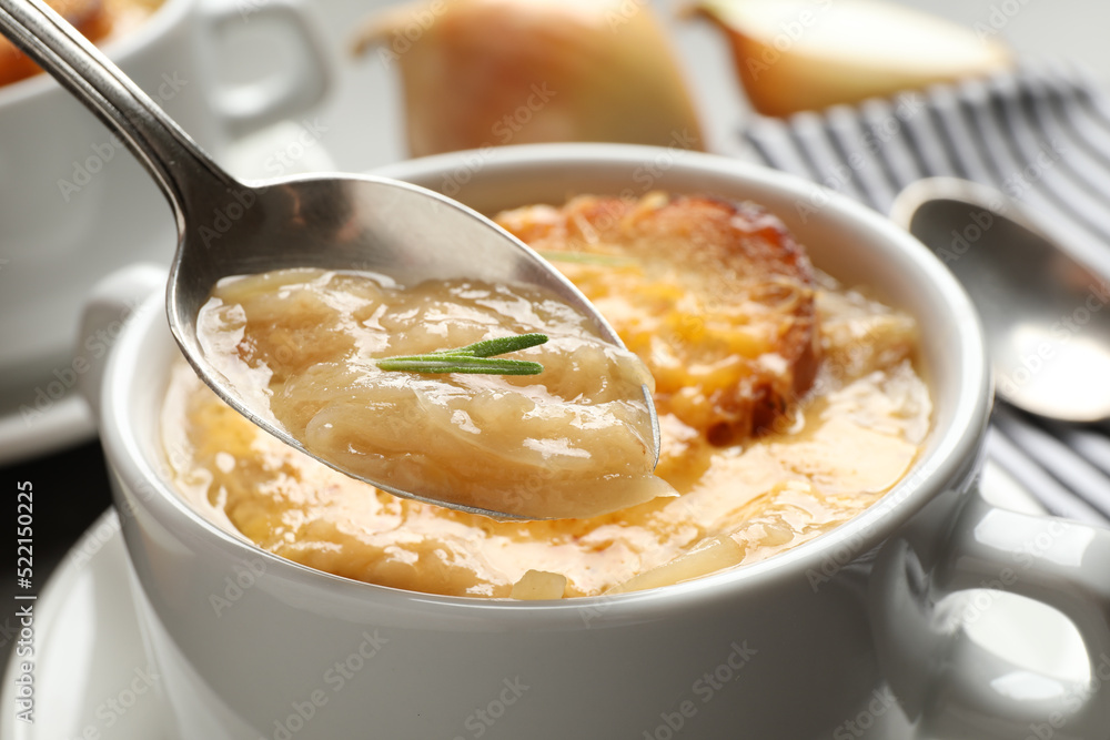 Spoon with fresh homemade homemade french onion soup over bowl, closeup Spoon with fresh homemade homemade french onion soup over bowl, closeup
