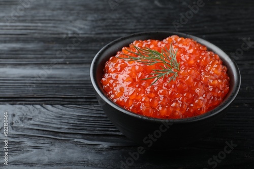 Bowl of delicious red caviar with dill on black wooden table, space for text