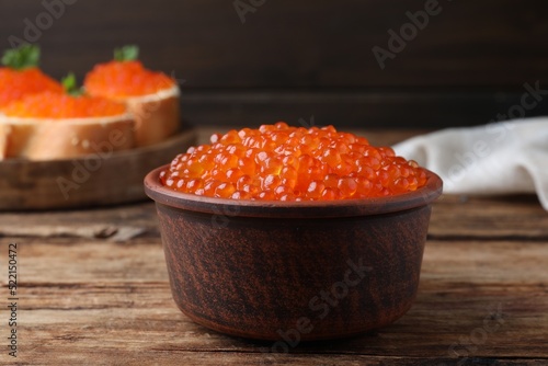 Bowl with delicious red caviar on wooden table