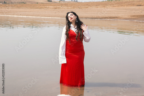 beautiful girl with long hair wearing red dress standing on the river photo