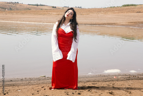 Young beautiful girl with long hair wearing red dress front of a river photo