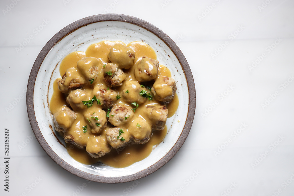 Swedish Meatball with brown mushroom sauce. Served on ceramic plate, on white table.