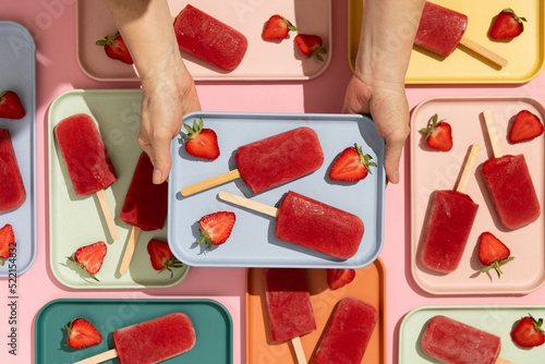 Woman holding strawberry ice cream popsicles on colorful tray photo