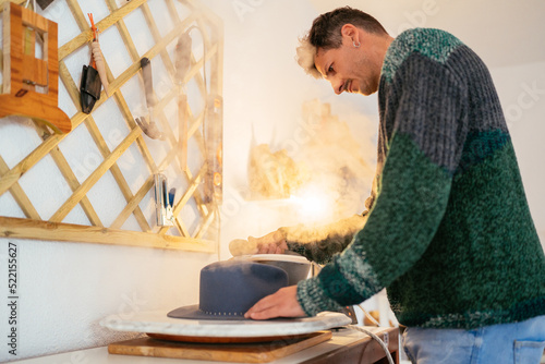 Skilled Hispanic hat maker ironing in workshop photo