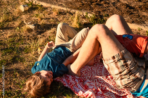 The kid playing outdoors with his dad, laying on a rug in a park  photo