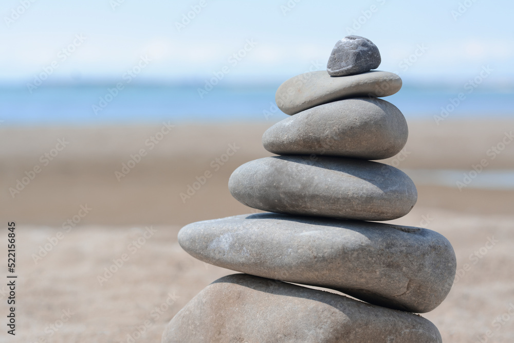 Fototapeta premium Stack of stones on beautiful sandy beach near sea, closeup. Space for text