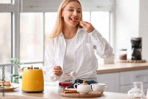 Mature woman eating tasty toasts in kitchen