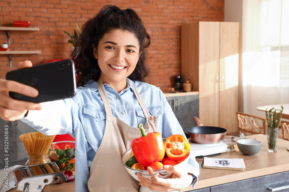 Young woman with colander and vegetables taking selfie in kitchen Young woman with colander and vegetables taking selfie in kitchen