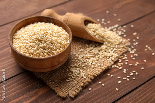 Bowl and scoop of sesame seeds on wooden background