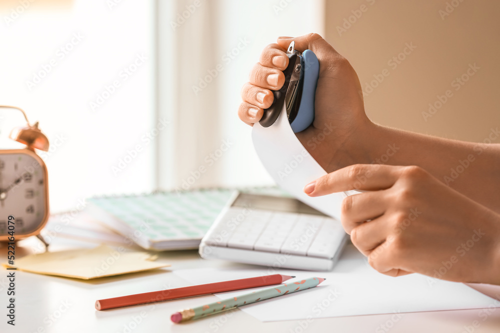 Fototapeta premium Woman with stapler and paper sheet at table, closeup