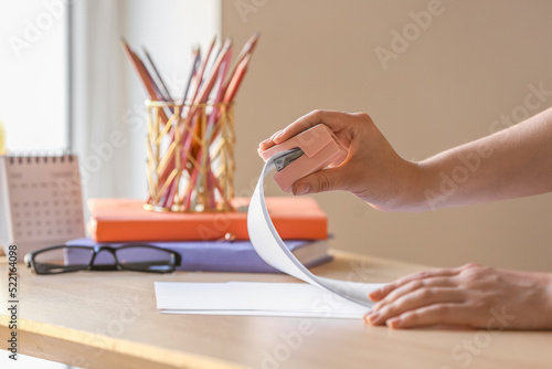 Woman with stapler and paper sheet at table, closeup photo