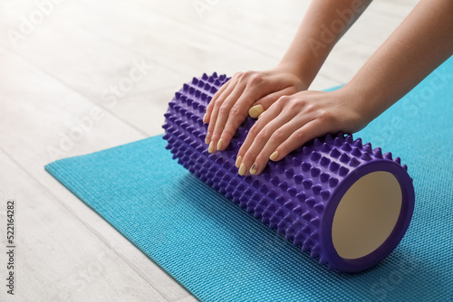 Woman training with foam roller on blue fitness mat at home, closeup photo