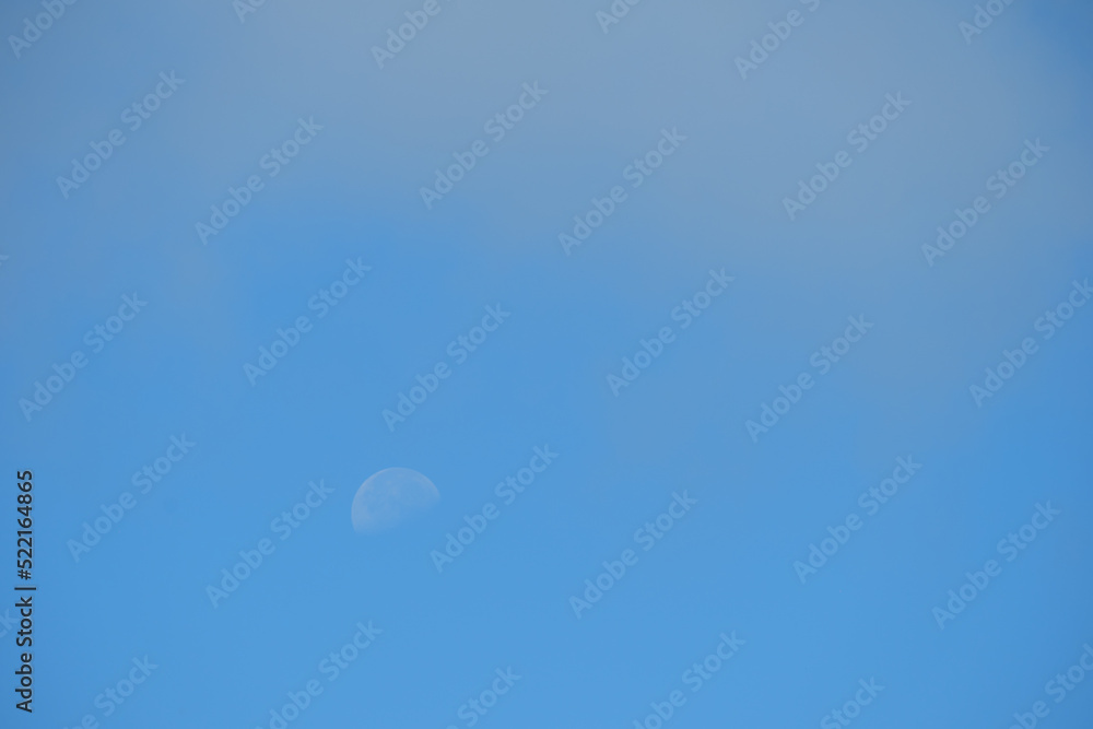 The daytime moon in the blue sky is covered with a light haze. The daytime moon in the blue sky is covered with a light haze.