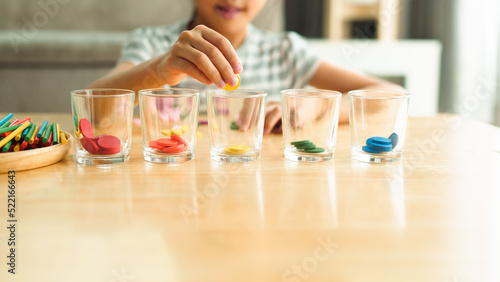 Unidentified kindergarten girl is learning to sorting the color coins to the glass, concept of homeschool, montessori, freedom, education, activity for child development and sensory activity for kid. photo