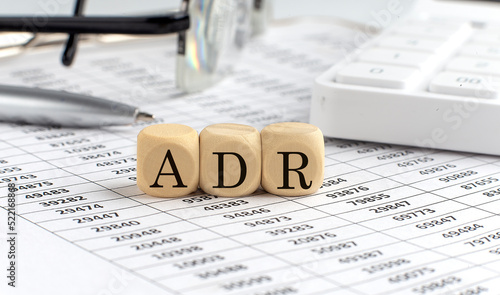 wooden cubes with the word ADR on a financial background with chart, calculator, pen and glasses, business concept.
