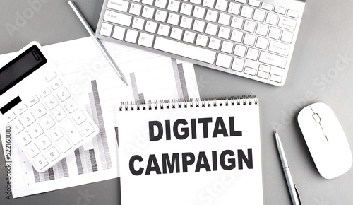 DIGITAL CAMPAIGN text written on notebook on grey background with chart and keyboard , business concept