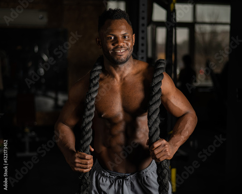 Muscular african american man posing with rope in gym. 