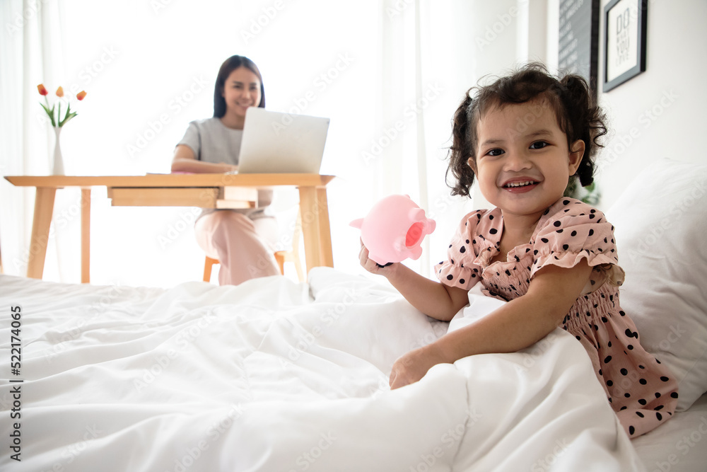 Happy loving family. Mother and her daughter child girl playing and working in bedroom. Little girl counting coins and saving money in pink piggy bank. Happy loving family. Mother and her daughter child girl playing and working in bedroom. Little girl counting coins and saving money in pink piggy bank.