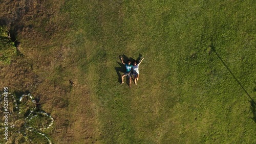 Two Happy Young People Lying On Grassy Field In Liloan, Southern Leyte, Philippines. - Drone Flying Upward photo