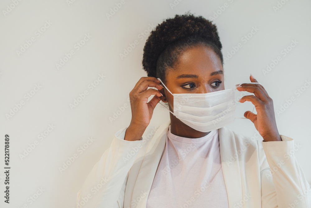 Close-up portrait of African American woman putting on facial mask looking away, posing against white background. Real people expression. Virus, epidemic Close-up portrait of African American woman putting on facial mask looking away, posing against white background. Real people expression. Virus, epidemic