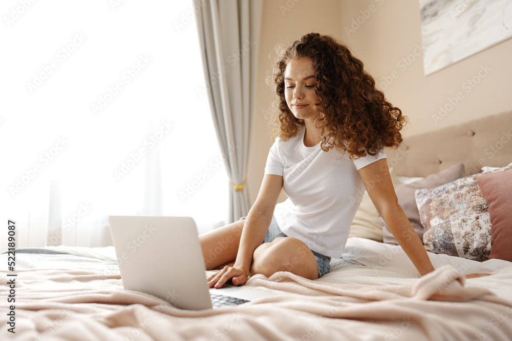 Portrait of a young curly woman using laptop in bed at home Portrait of a young curly woman using laptop in bed at home