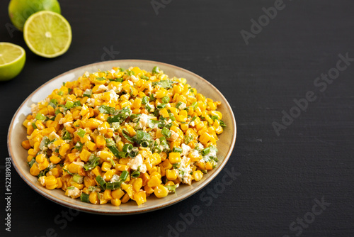 Homemade Mexican Street Corn Esquites on a Plate on a black background, side view. Copy space.