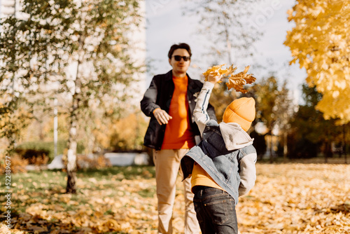 Father and son having fun in autumn park with fallen leaves, throwing up leaf. Child kid boy and his dad outdoors playing with maple leaves © Anna