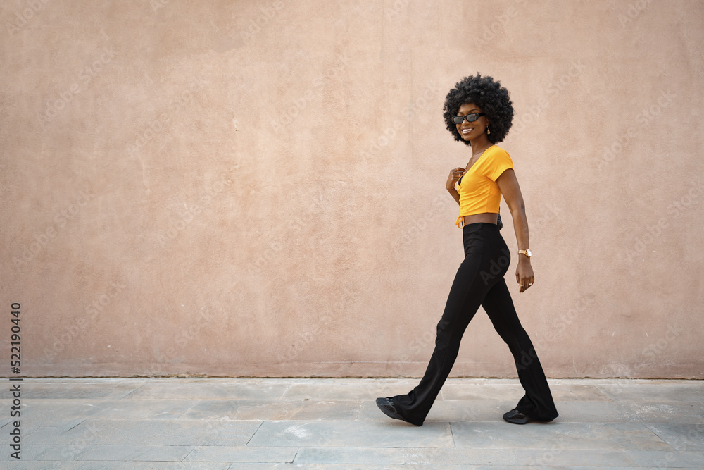 Fototapeta premium Smiling fashionable afro american woman walking on city street
