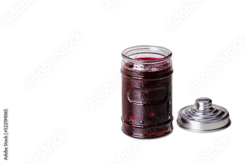 Open glass jar with cherry jam on a white background. There is a jar lid next to it.