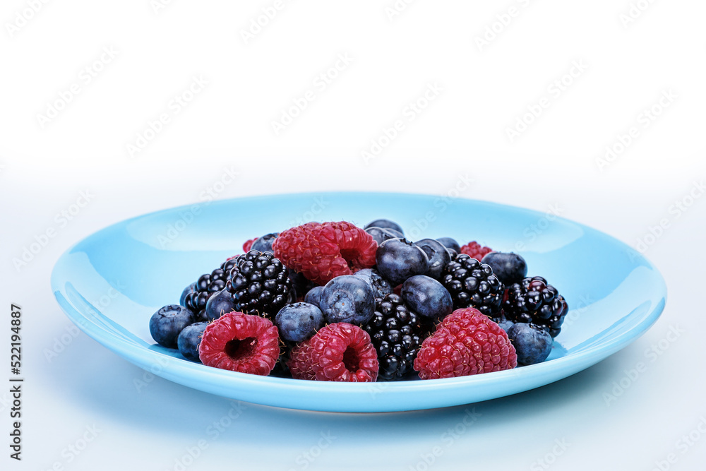 Blue plate with summer raspberries, blueberries and mulberries lying in it