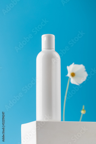  An empty bottle with a cosmetic product on a pedestal on a blue background. Micellar water, facial cleansing lotion.